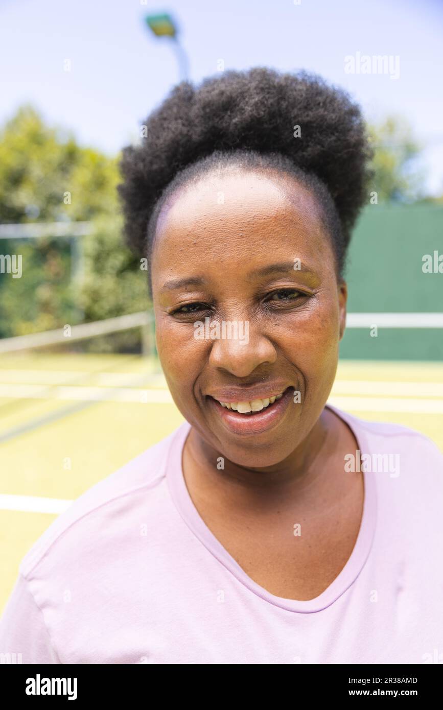 Retrato de la mujer afroamericana mayor feliz sonriendo en la pista de tenis de hierba soleada Foto de stock