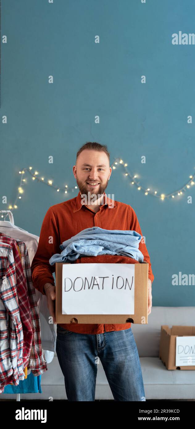 Hombre sonriente con la caja de la donación llena de ropa usada vieja para la gente pobre y necesitada. Concepto de donación y caridad Foto de stock