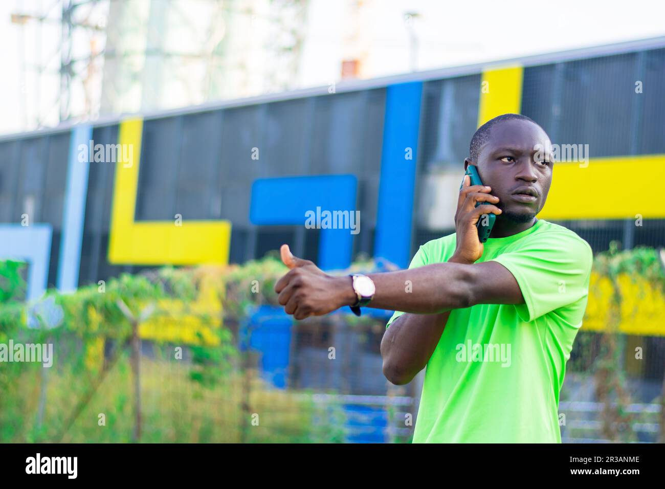 Un joven negro está contemplado, absorto en su teléfono móvil y en el mundo de la tecnología inalámbrica. aislado en una ciudad urbana borrosa Foto de stock