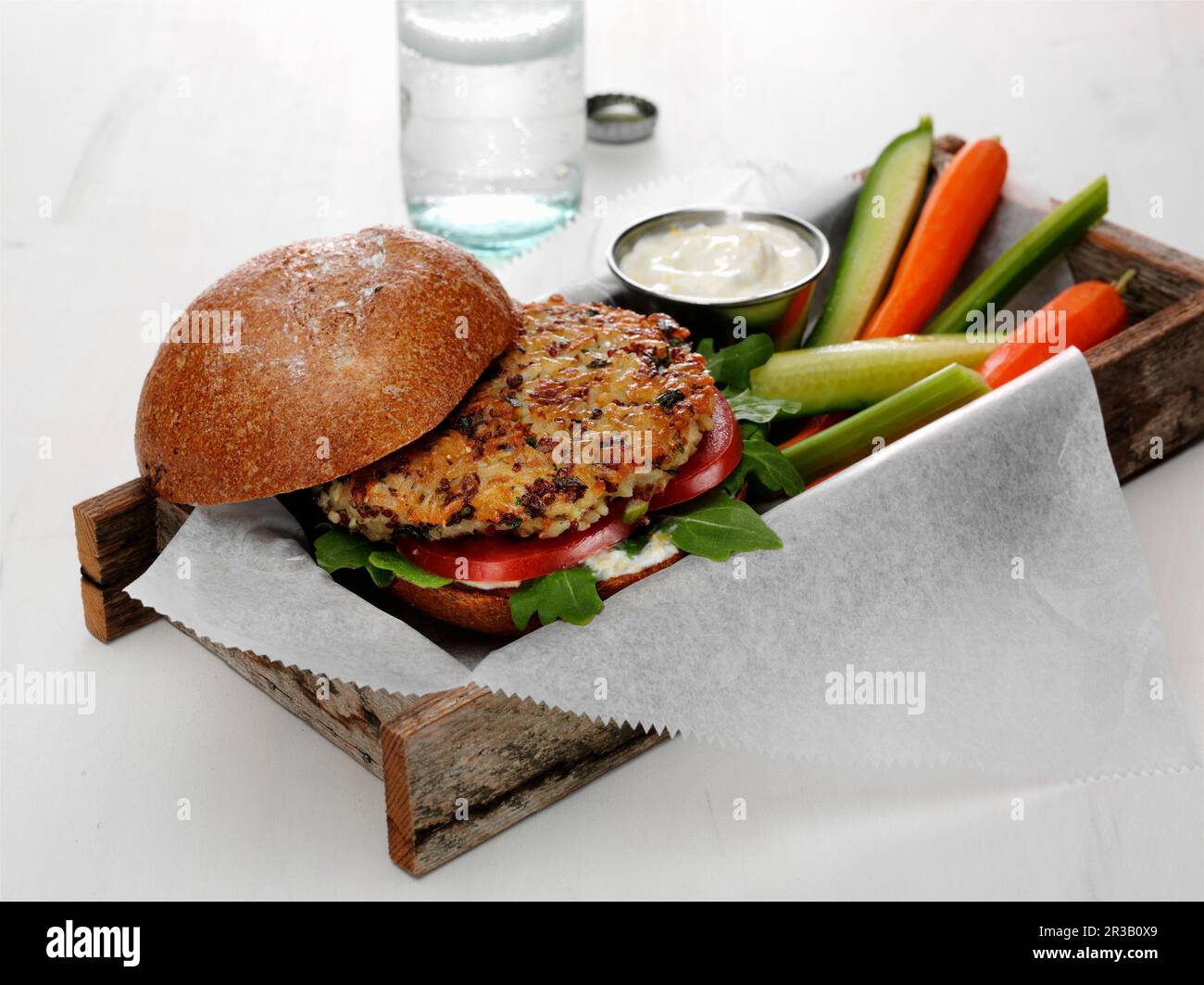 Quinoa y hamburguesa de arroz integral con tomate y espinaca bebé en un bollo con lanzas vegetales Foto de stock