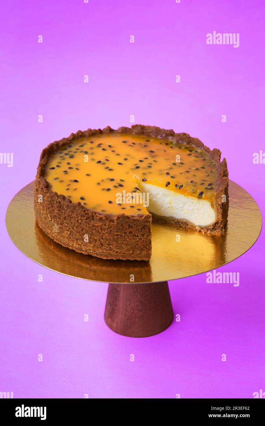 Pastel de cumpleaños en rodajas en el soporte de pastel de madera. Hermosa  tarta de queso con pasionfruit. Fondo morado. Espacio de copia. Fotografía  de alimentos para recetas Fotografía de stock -