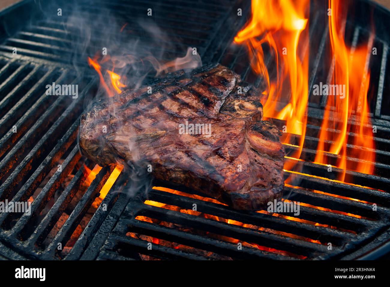 Bistec a la parrilla en parrilla de barbacoa con carbón en llamas