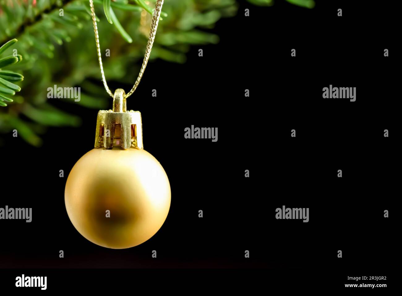 Bola amarilla en una rama verde de un árbol de Navidad aislado en un fondo negro Foto de stock
