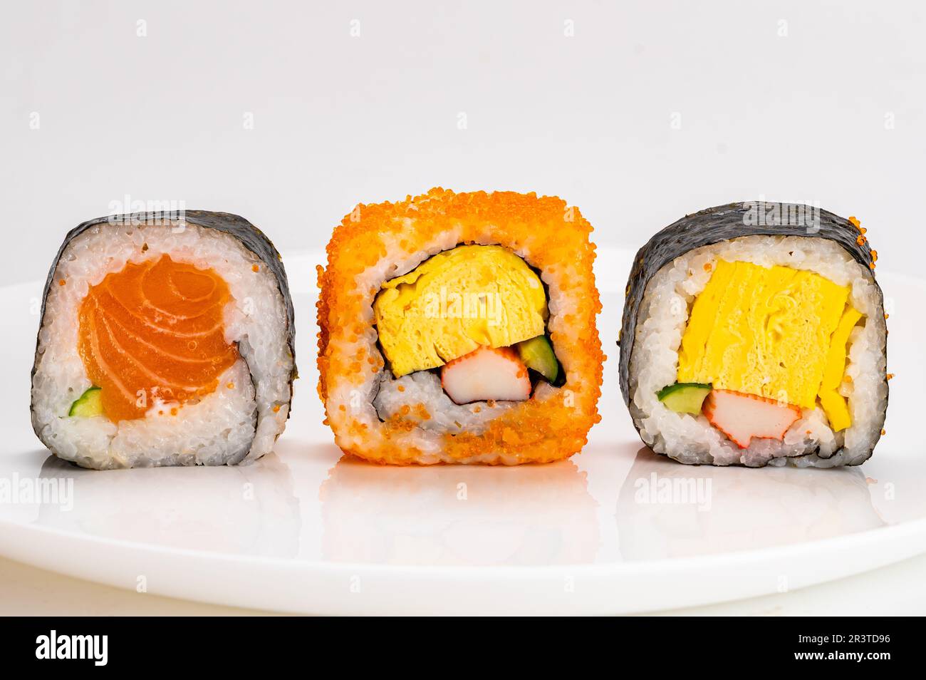 Varios rollos de sushi sashimi de estilo japonés casero, algas nori, pescado salmón, en placa de cerámica blanca aislada sobre fondo blanco. Foto de stock