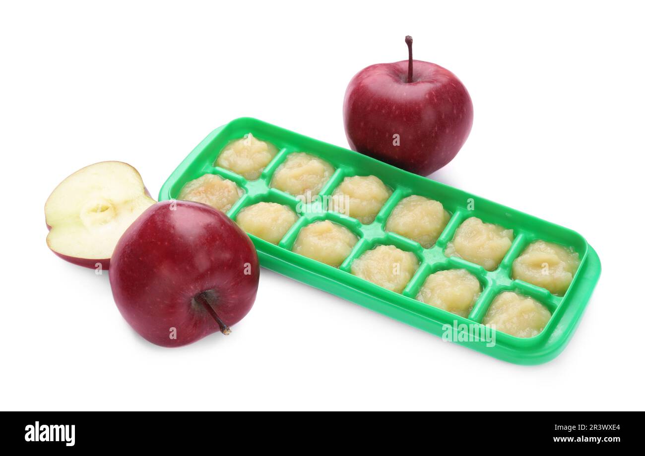 Puré de manzana en bandeja de cubitos de hielo y frutas de manzana frescas aisladas en blanco. Listo para congelar Foto de stock