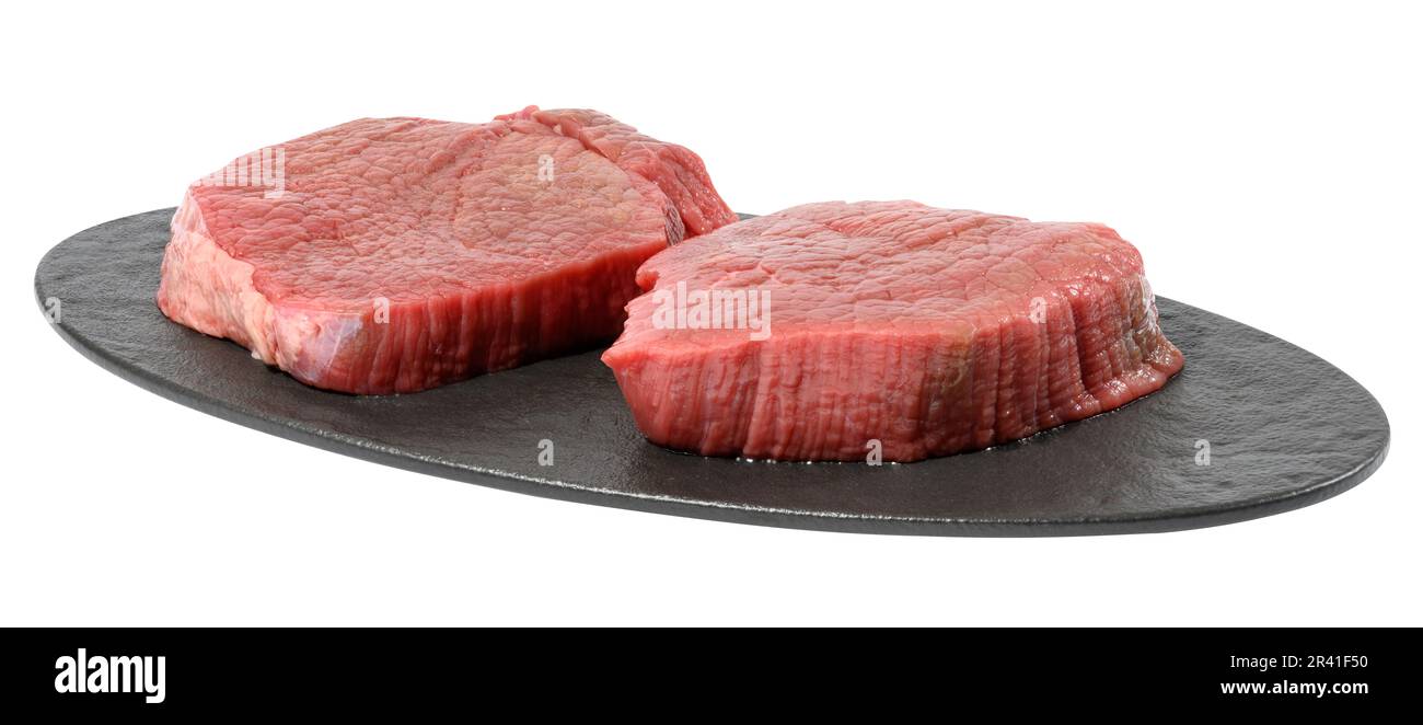 Dos filete de carne cruda redonda en una tabla de cortar oval negro, fondo aislado blanco Foto de stock