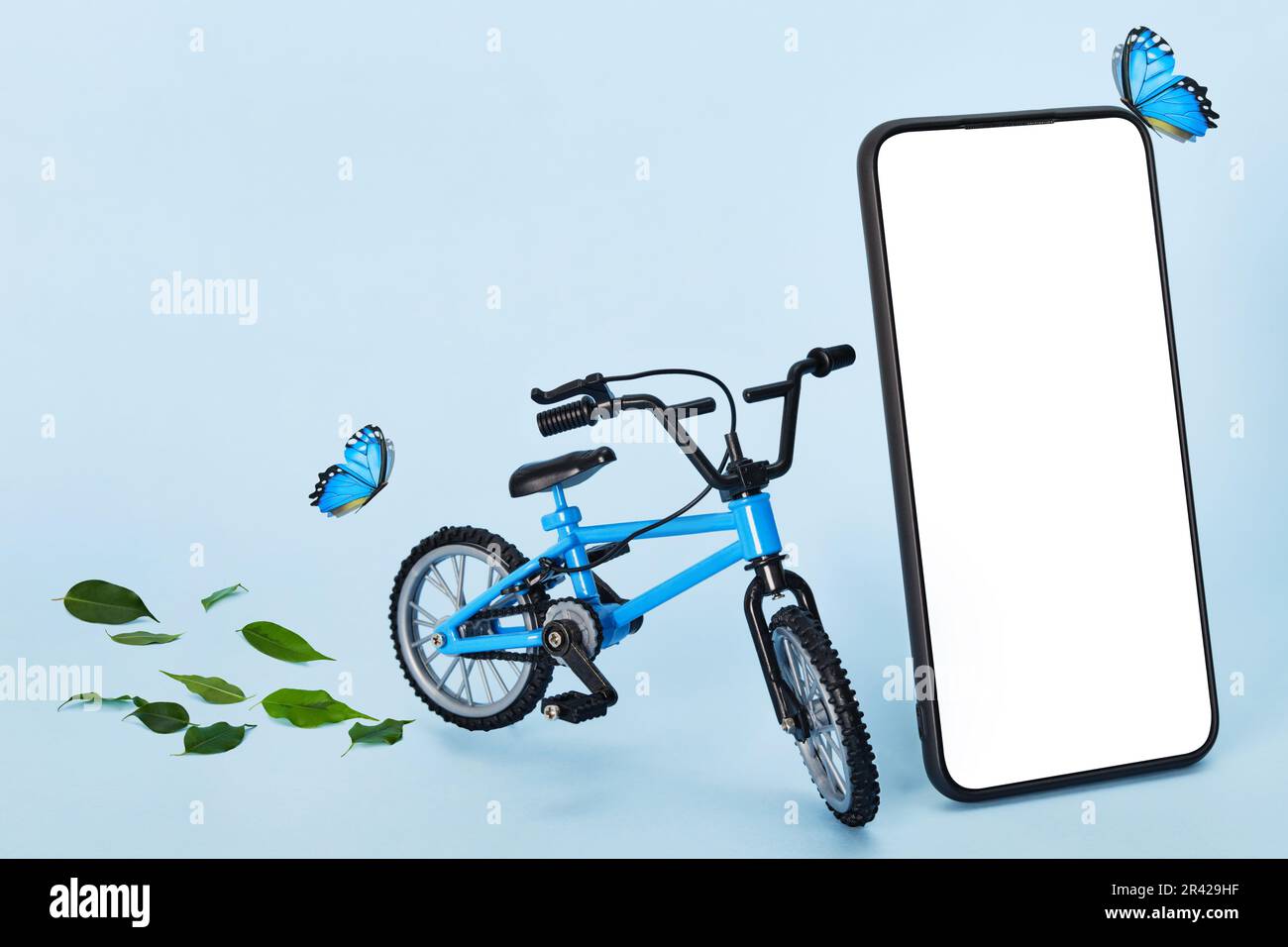 Concepto de entrega ecológica creativa. Smartphone con espacio de copia, bicicleta y mariposas sobre fondo azul. Servicio de mensajería sostenible Foto de stock