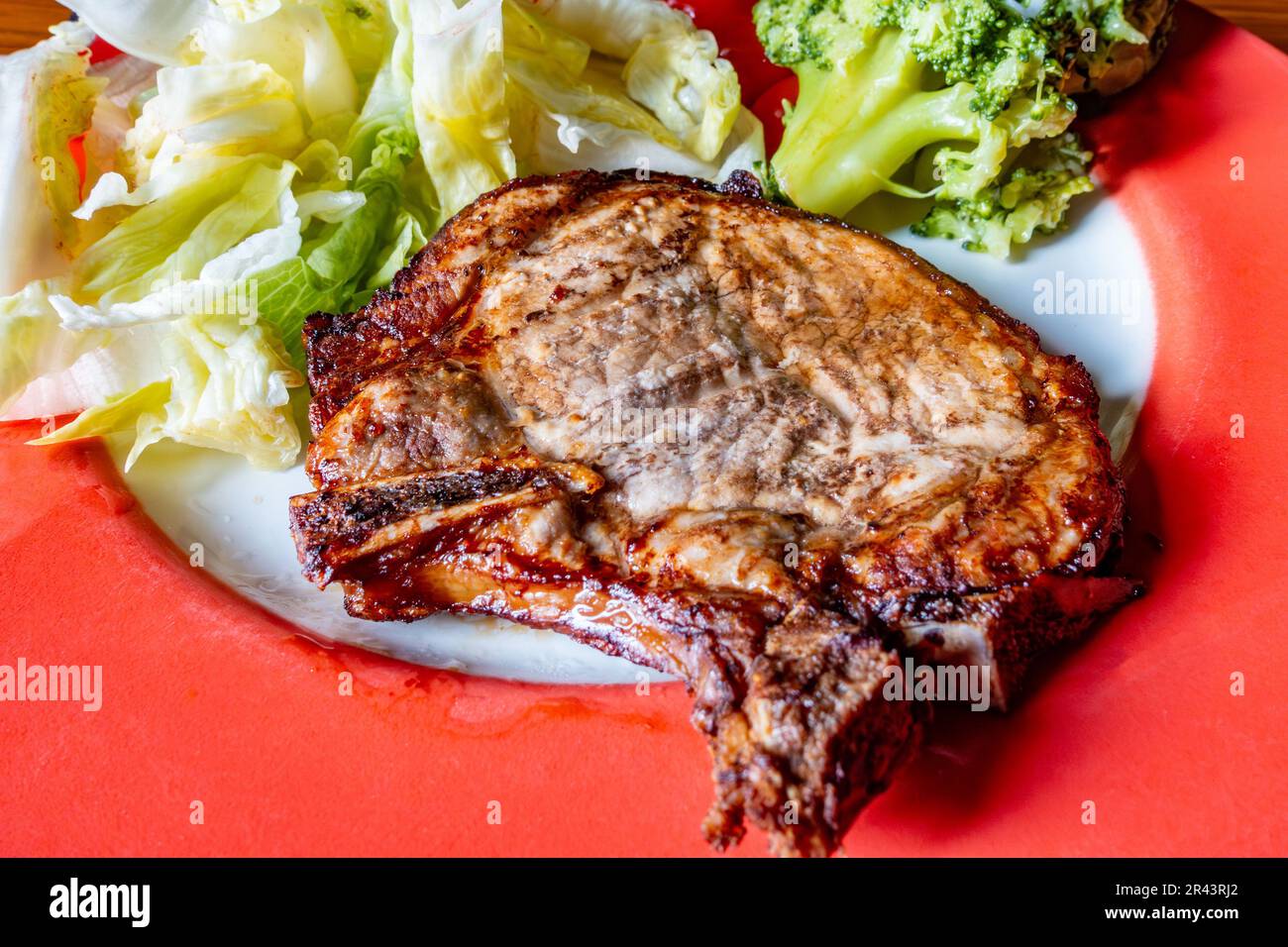 Una chuleta de cerdo frita al aire servida con brócoli al vapor y ensalada en una comida baja en carbohidratos Foto de stock