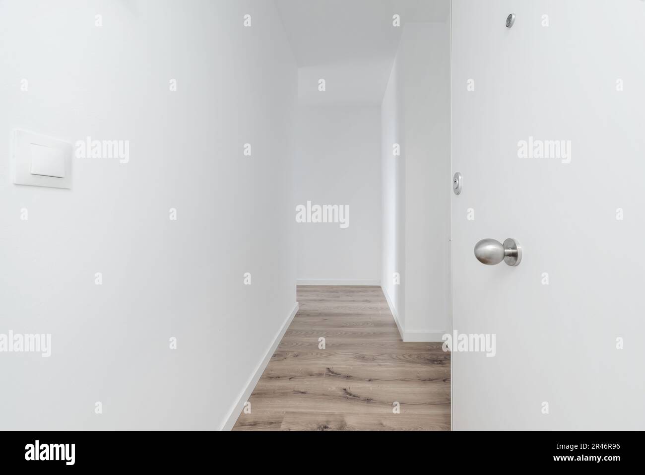 Salón de una casa de reciente construcción con una puerta blindada blanca, paredes  blancas lisas y suelos de madera Fotografía de stock - Alamy