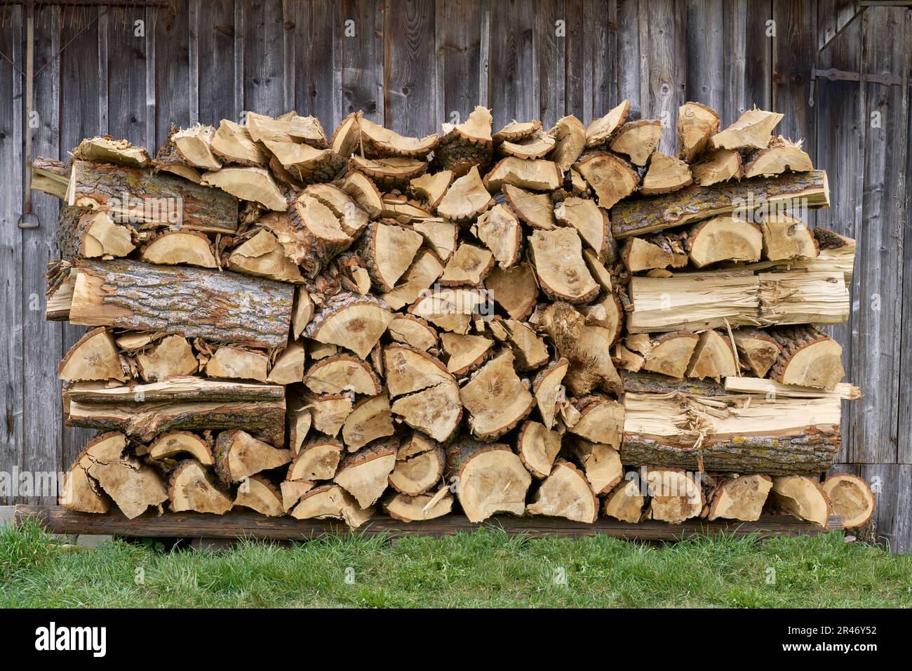 Pila de madera rústica en la hierba frente a la pared de madera de un granero Foto de stock
