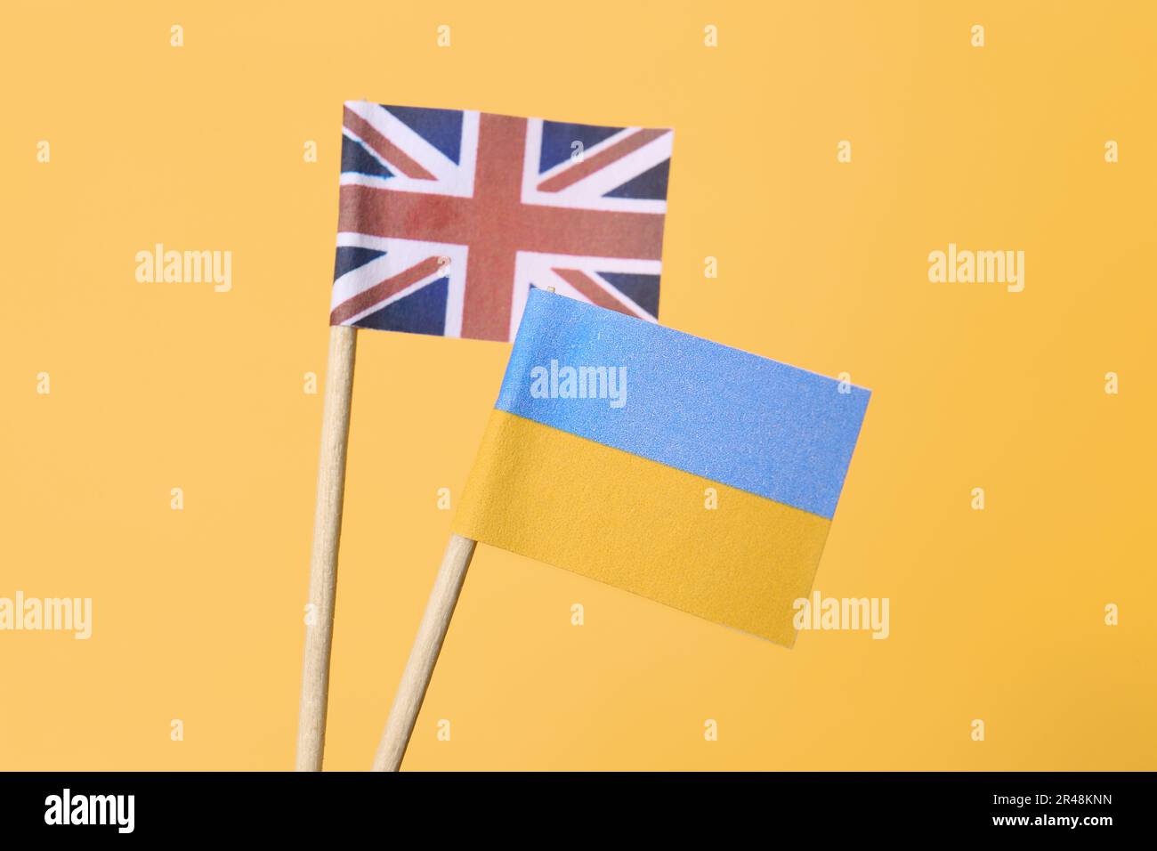 Pequeñas banderas de papel de Ucrania y Reino Unido sobre fondo naranja, primer plano Foto de stock