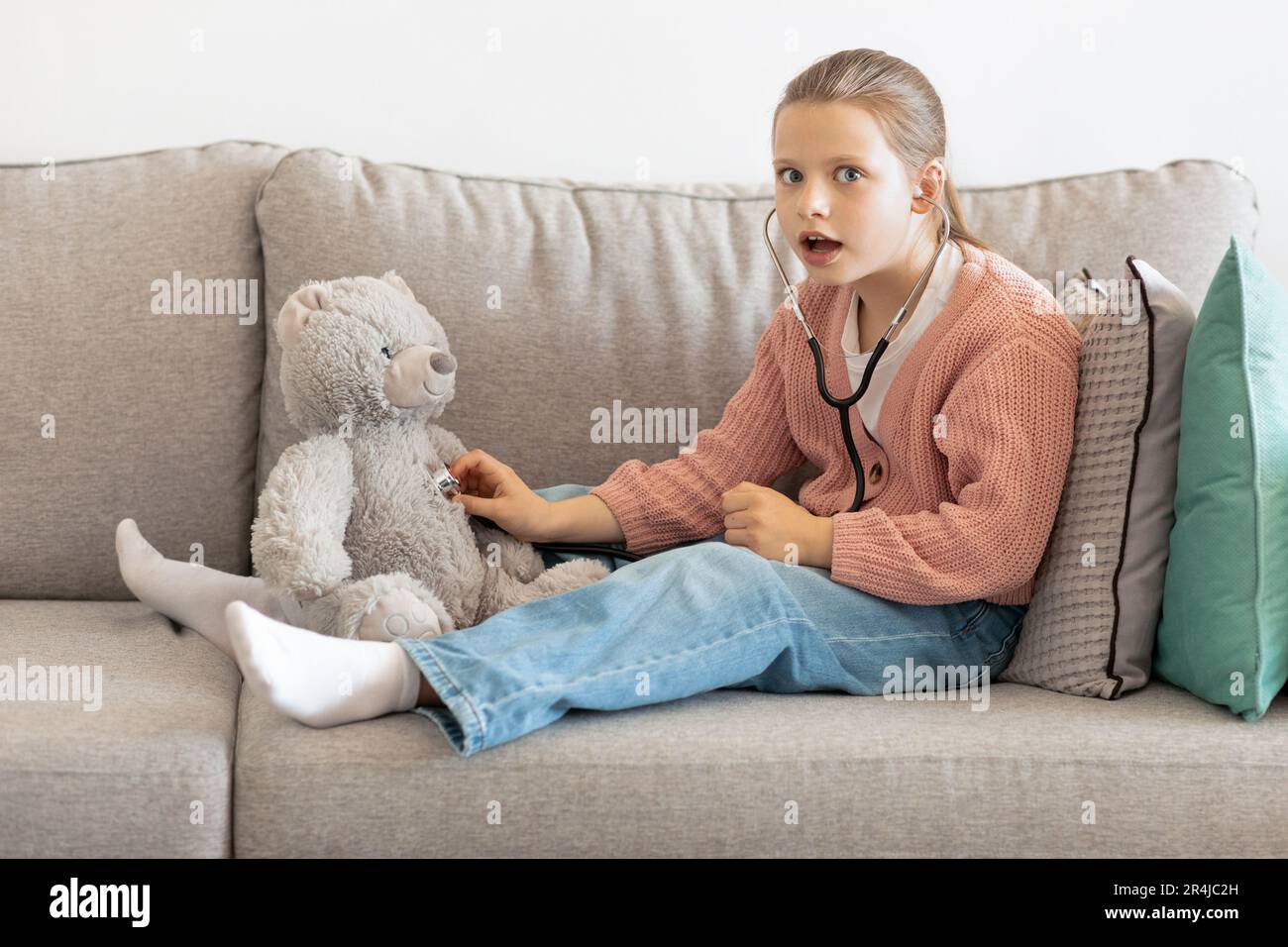 Chocada divertida niña caucásica jugando médico con oso de juguete, escucha  respirar con estetoscopio Fotografía de stock - Alamy