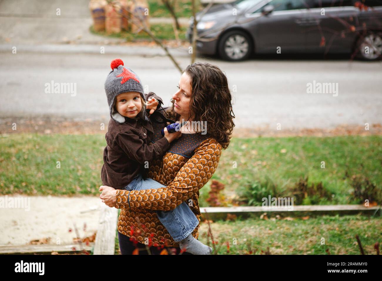 Una mamá se para en su patio con ternura sosteniendo a un niño sonriente en sus brazos Foto de stock