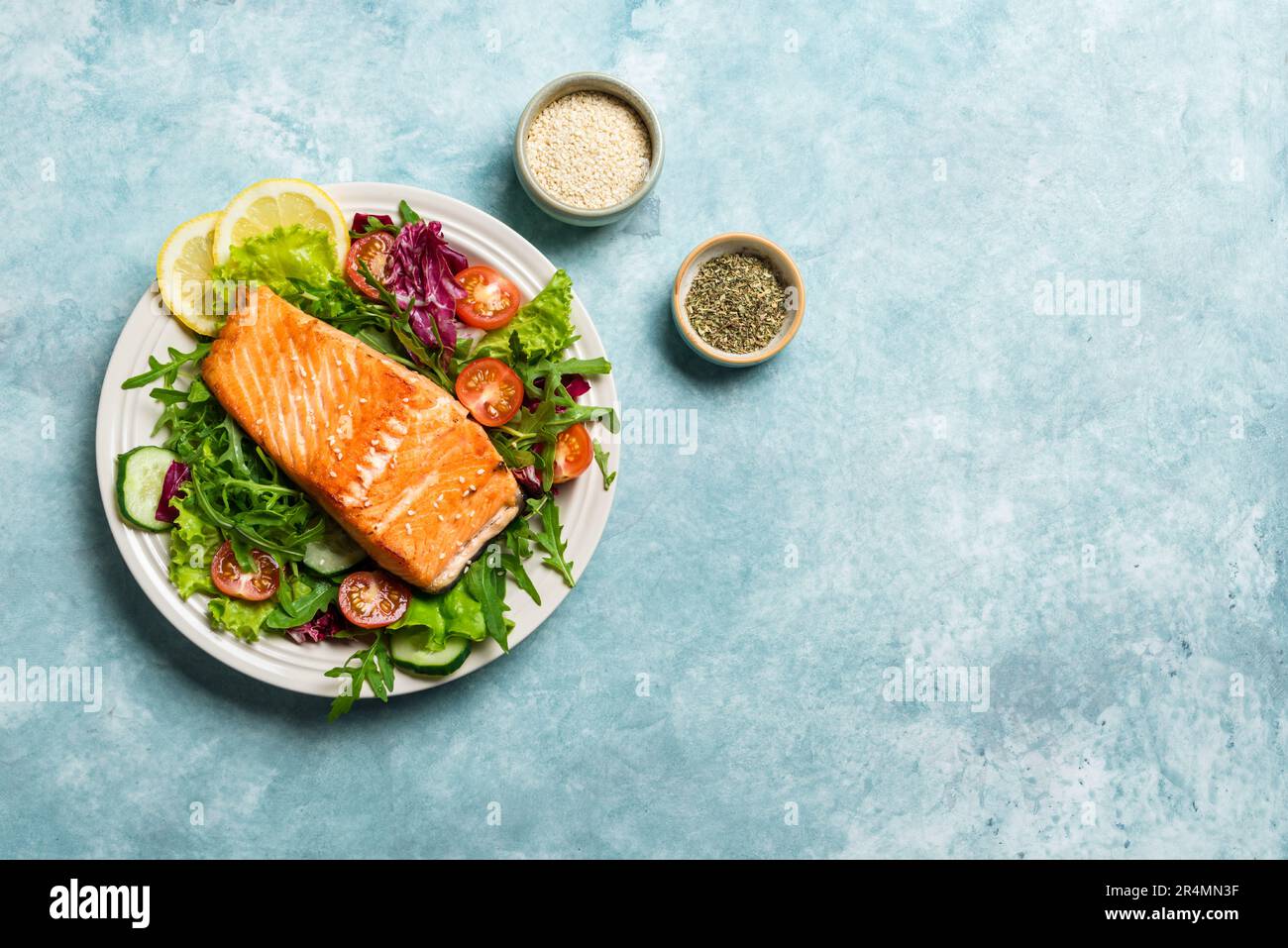 Filete de salmón a la parrilla y ensalada de verduras frescas con tomate, lechuga, rúcula. Comida sana - ensalada verde y salmón asado sobre fondo azul, Foto de stock
