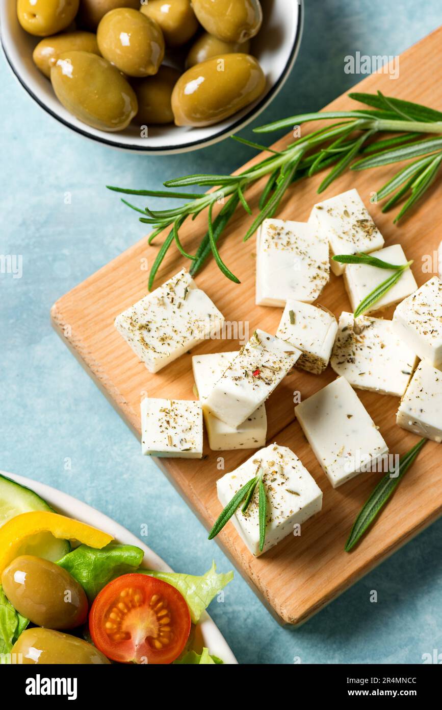 Ingredientes saludables para cocinar ensalada - queso feta, aceitunas y aceite de oliva. Comida griega mediterránea. Queso feta de cabra picado con hierbas de romero. Foto de stock