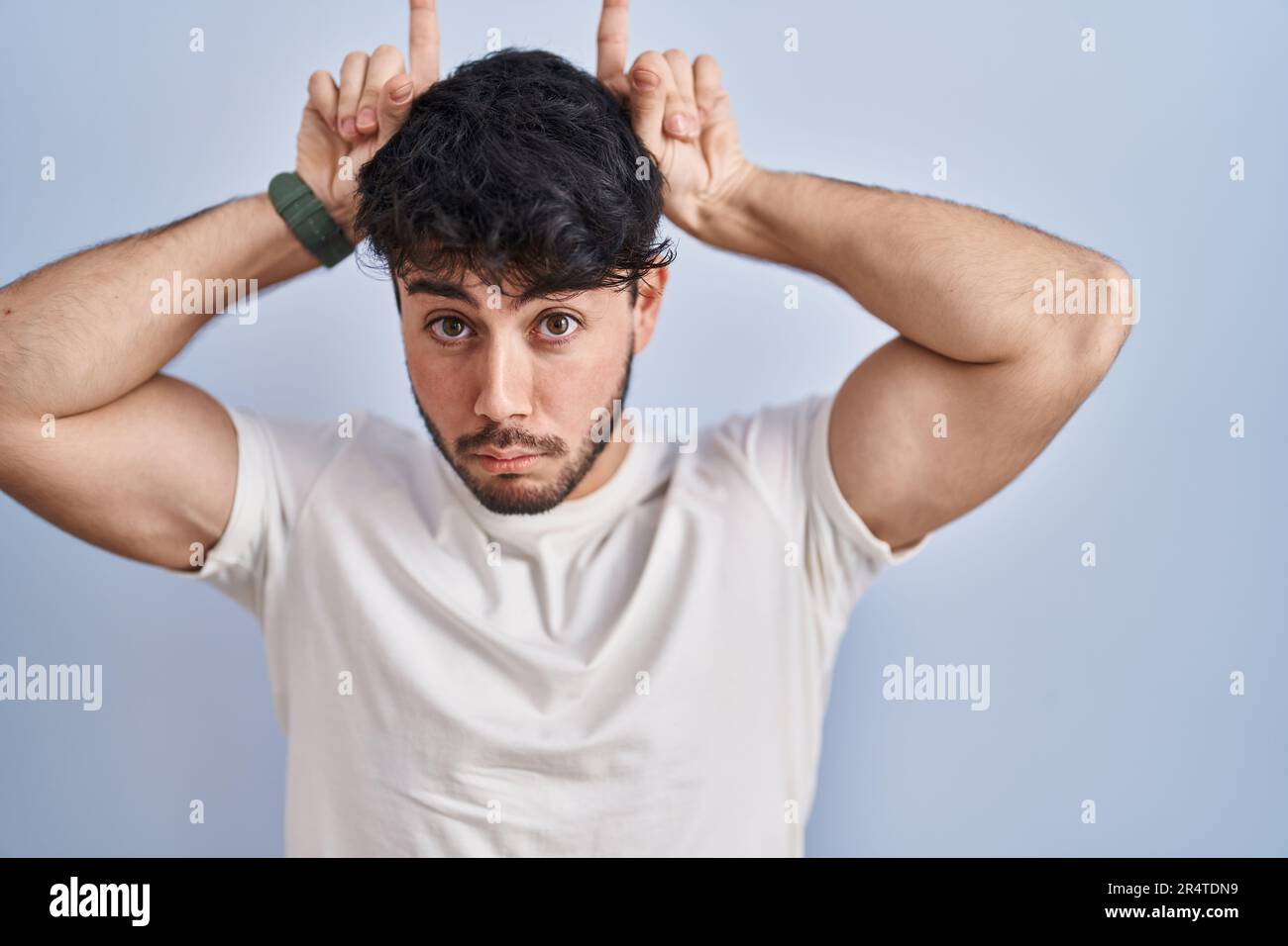 Hombre hispano con barba de pie sobre fondo blanco haciendo un gesto