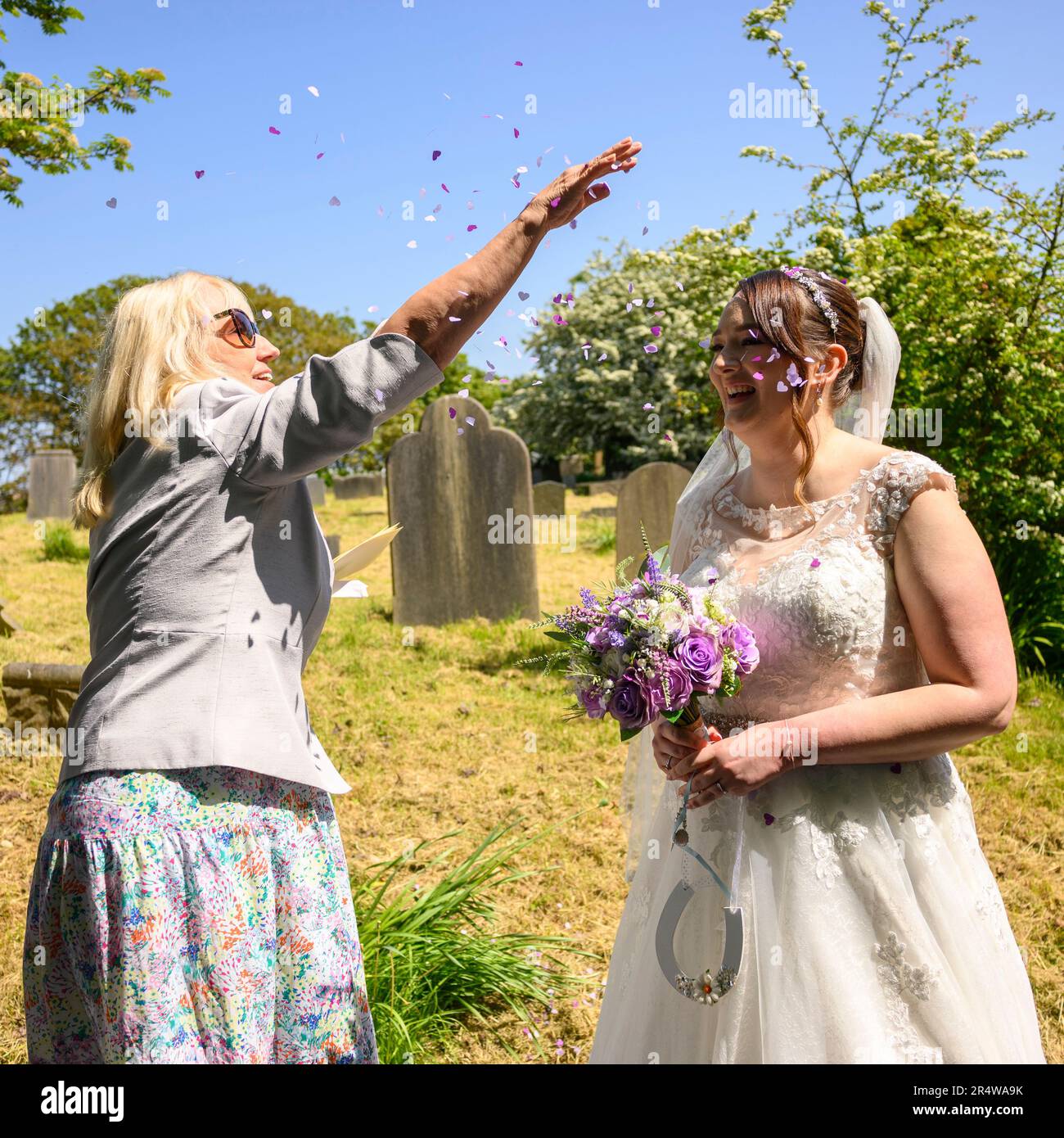 Mujer lanzando confeti sobre una novia en un vestido de novia el día de la boda Foto de stock