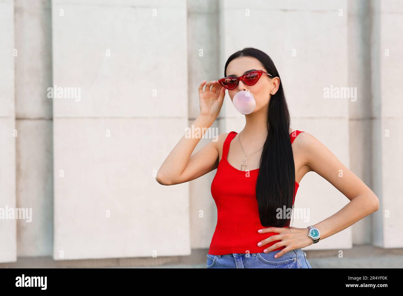 Mujer hermosa en gafas de sol elegantes que soplan goma cerca de la pared al aire libre, para el Fotografía de stock - Alamy