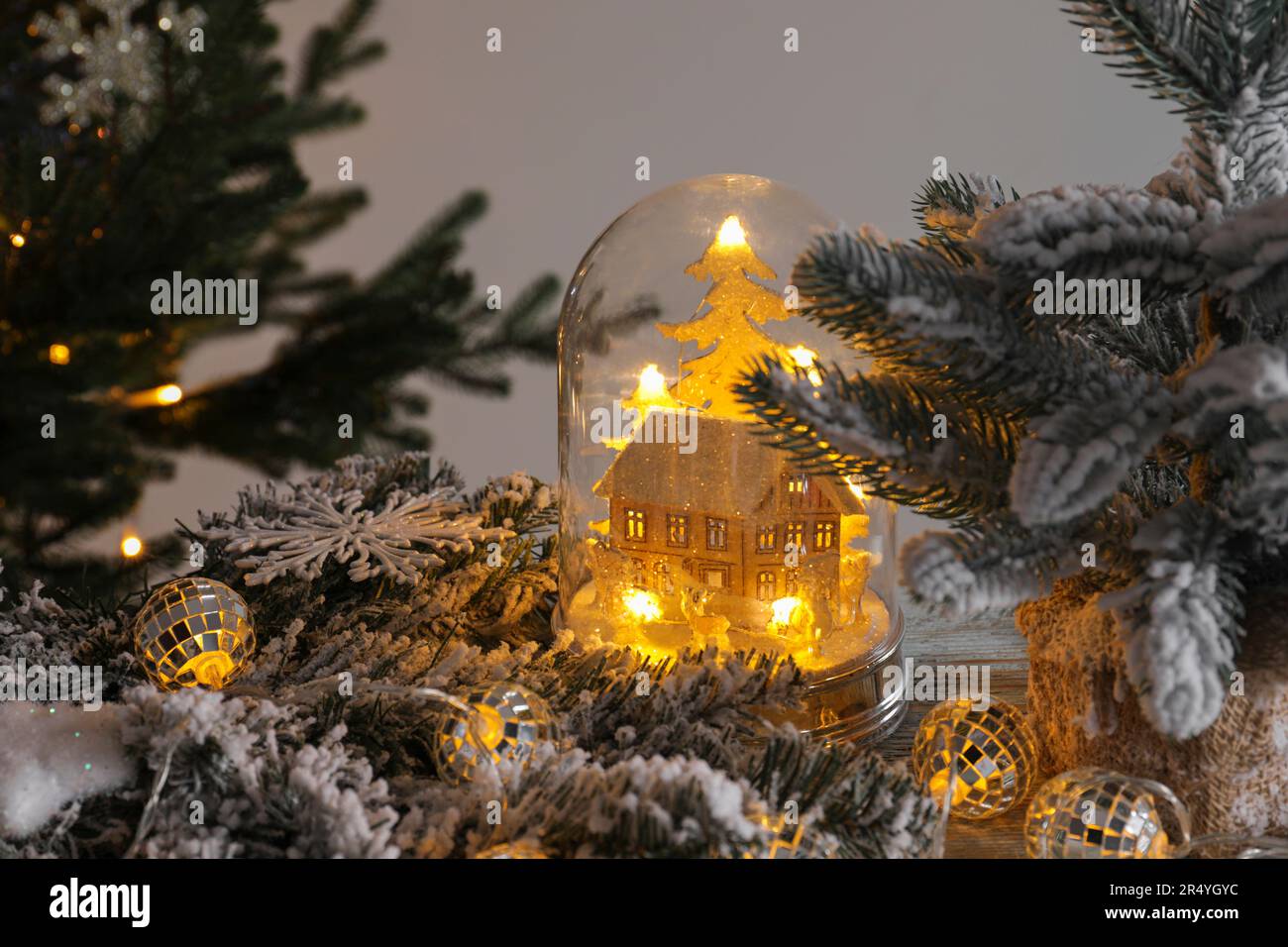 Hermoso globo de nieve con modelo de casa, luces de hadas brillantes en el interior y decoración de Navidad en la mesa de madera Foto de stock