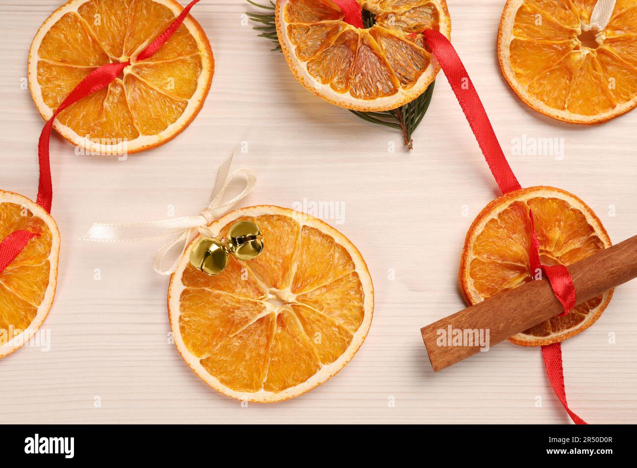 Hermosa guirnalda con naranjas secas, canela, cinta y campanas de trineo en la mesa de madera blanca, tendido plano Foto de stock