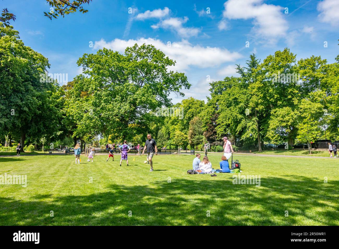 Una vista de la gente disfrutando de Alexandra Gardens, un parque público en Windsor, Berkshire, Reino Unido con árboles verdes, hierba y cielo azul Foto de stock