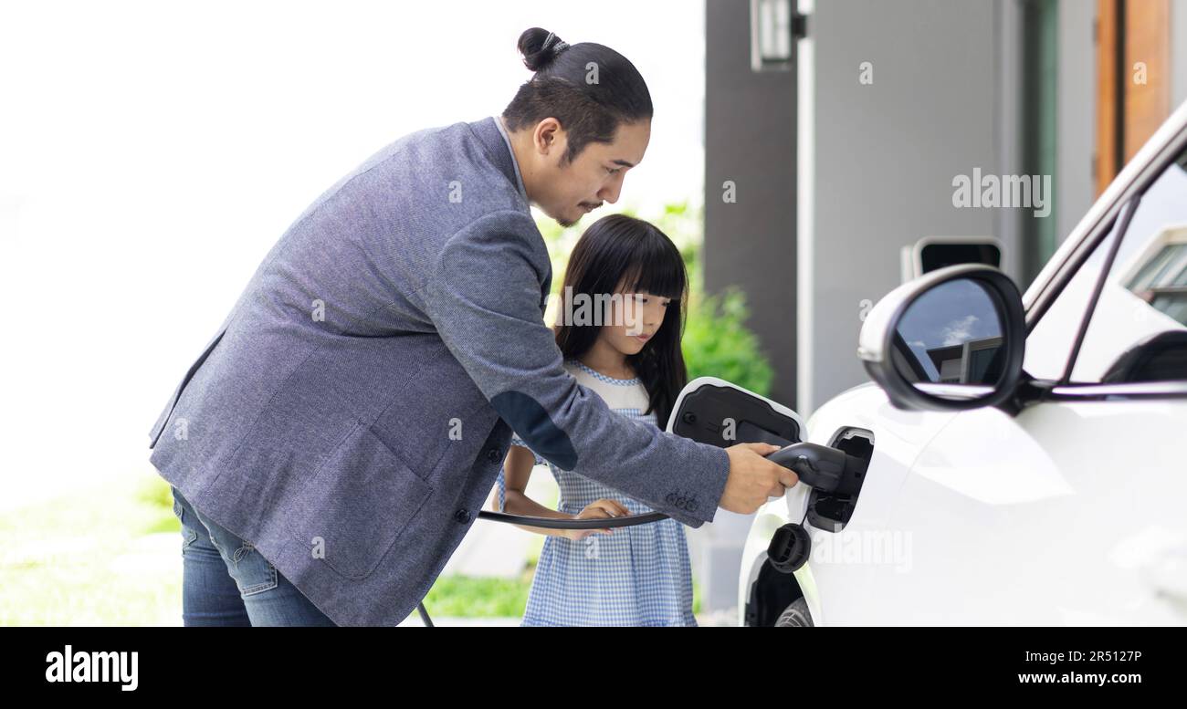 El padre y la hija progresivos enchufan el cargador EV de la estación de carga casera al vehículo eléctrico. Futuro coche ecológico con coches EV impulsados por Foto de stock