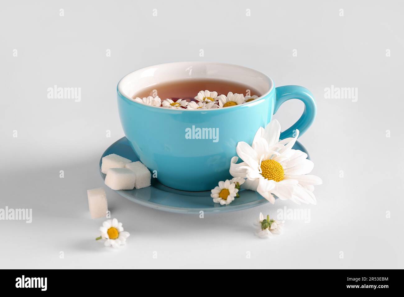 Taza de té de manzanilla natural y flores en la mesa blanca cerca