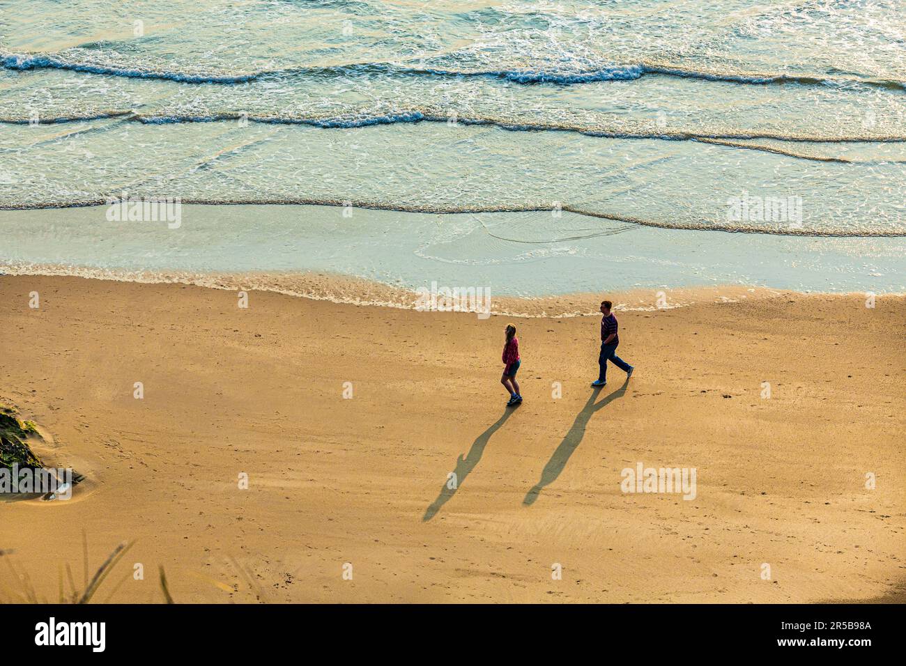 Pareja joven caminando al atardecer en la playa de Whitesands Bay, una playa con bandera azul, península de St David, Parque Nacional de la Costa de Pembrokeshire, Gales del Oeste Foto de stock