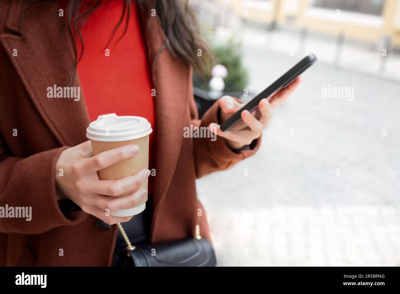 La mujer usa el teléfono móvil en la calle y toma café. Foto de stock