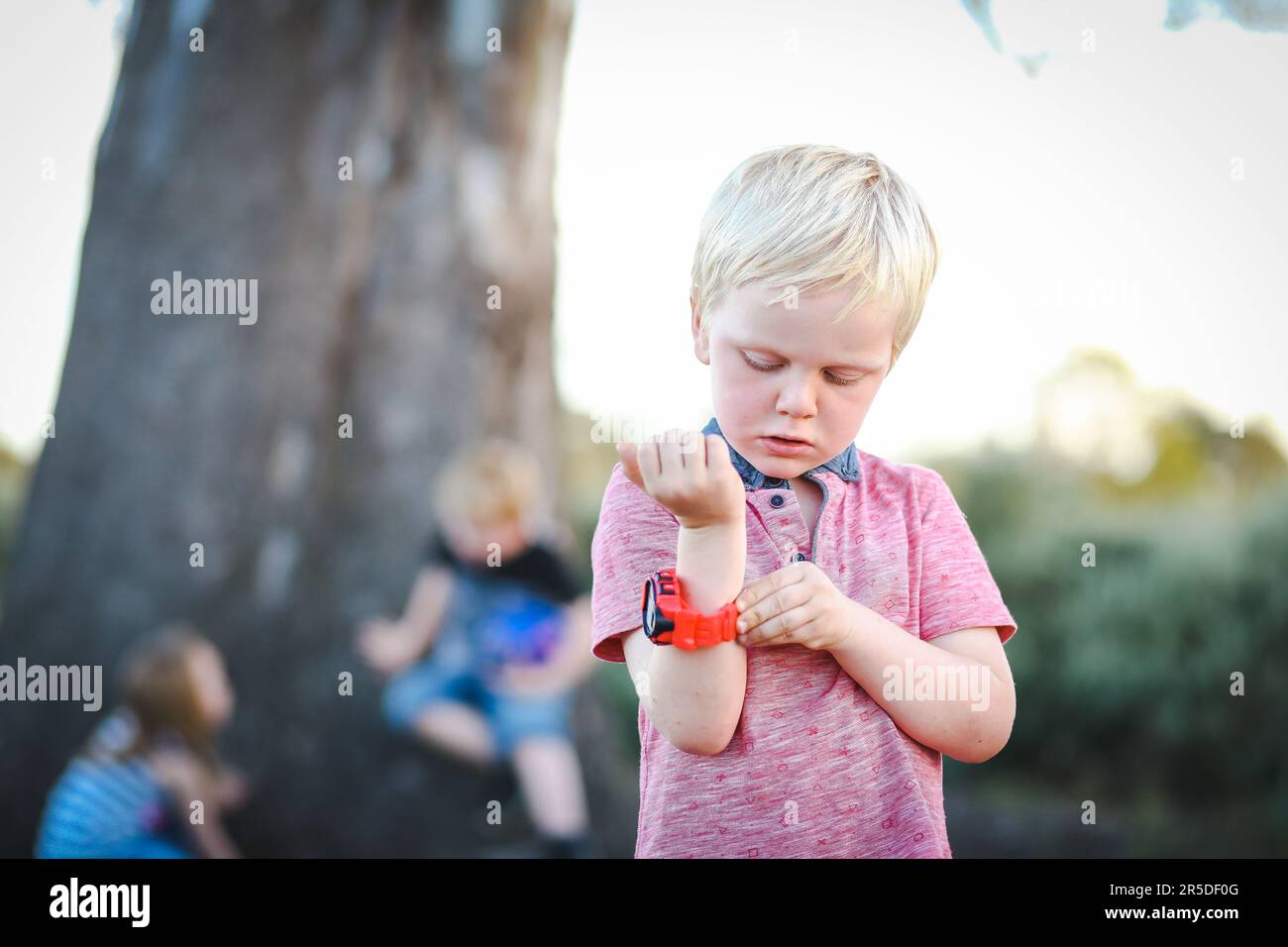 Niño pequeño con reloj rojo brillante en el parque con otros niños jugando  en el fondo Fotografía de stock - Alamy