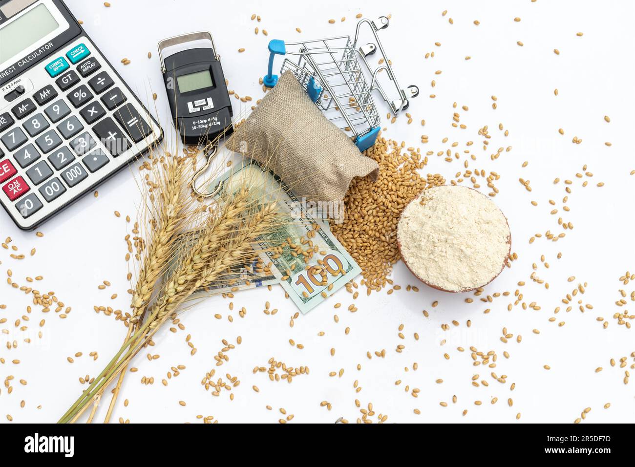 Granos de trigo y harina con escala de ponderación y calculadora con billetes de dólares estadounidenses sobre fondo blanco Foto de stock