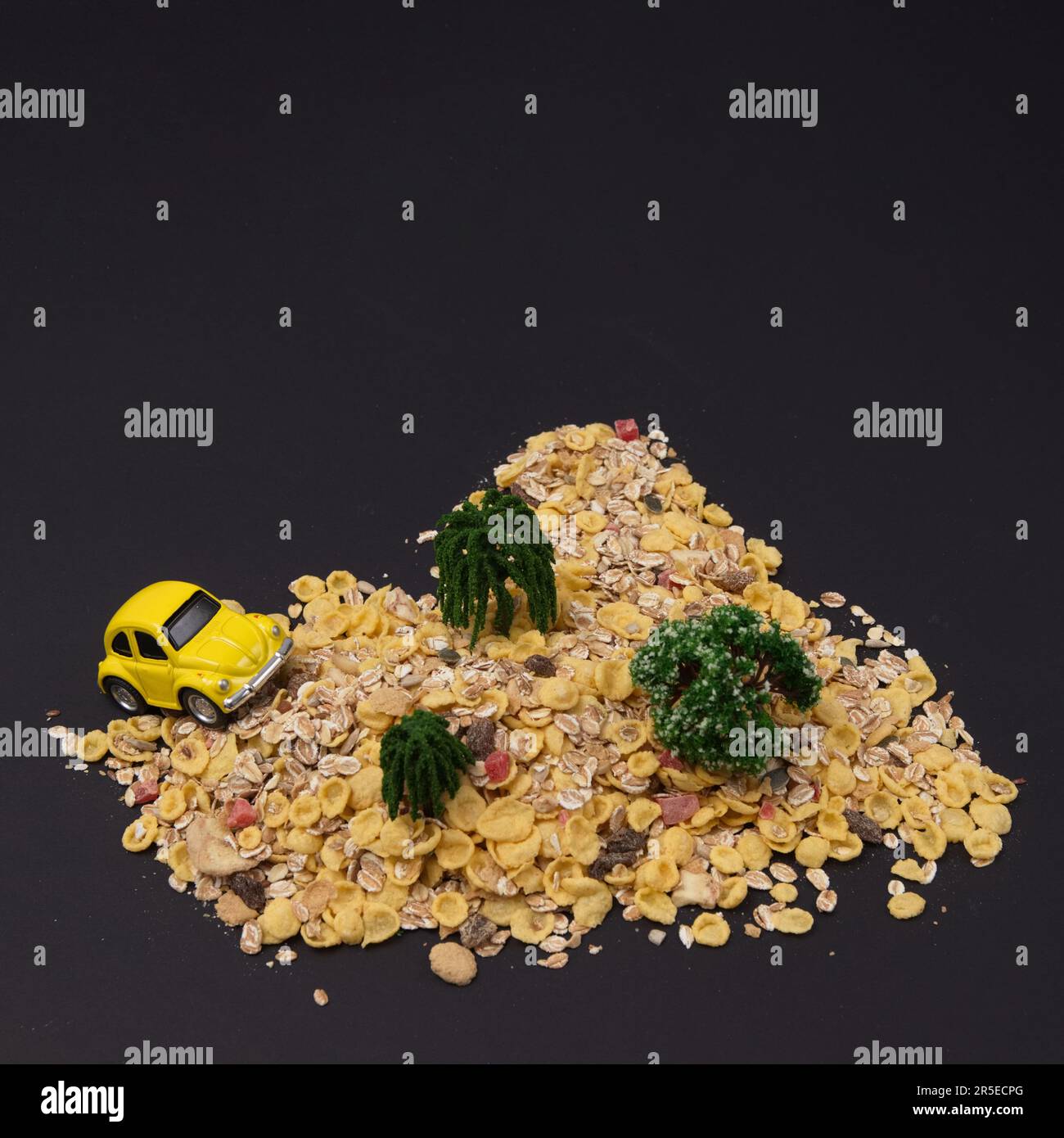 Escarabajo amarillo sube una montaña de copos de maíz con árboles sobre un fondo negro. Concepto de estilo de vida mínimo. Foto de stock