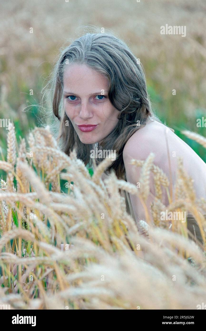 mujer de pelo rubia bonita delgada joven en sus primeros 20s posando para el retrato en campo de trigo 1990s Foto de stock