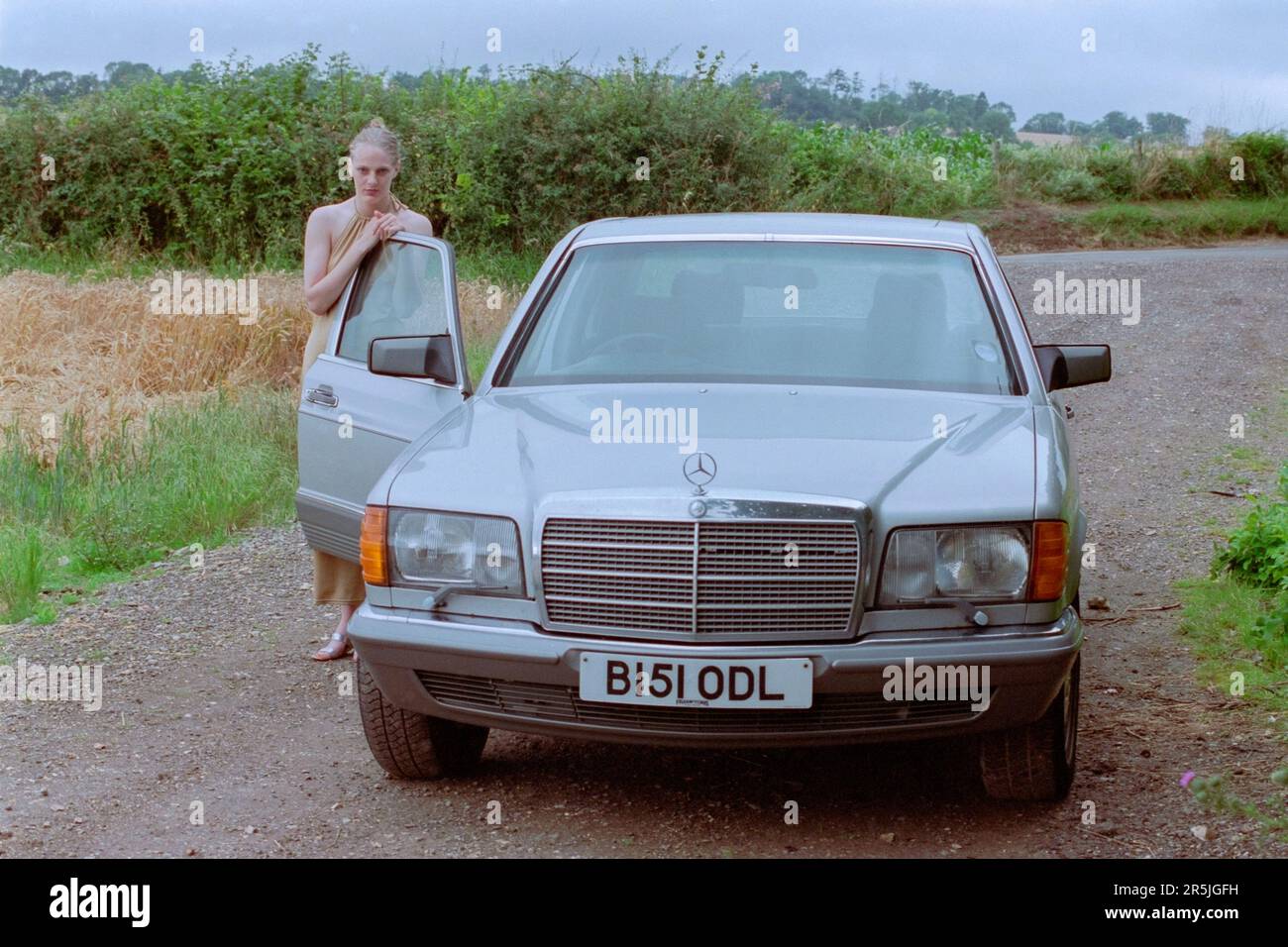 mujer de pelo rubio guapa delgada joven en sus 20s años posando para el retrato junto a mercedes 280 sel car country lane 1990s inglaterra Foto de stock