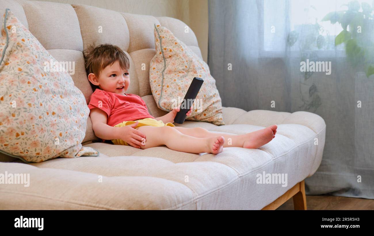 El niño alegre está sentado en el sofá sosteniendo el control