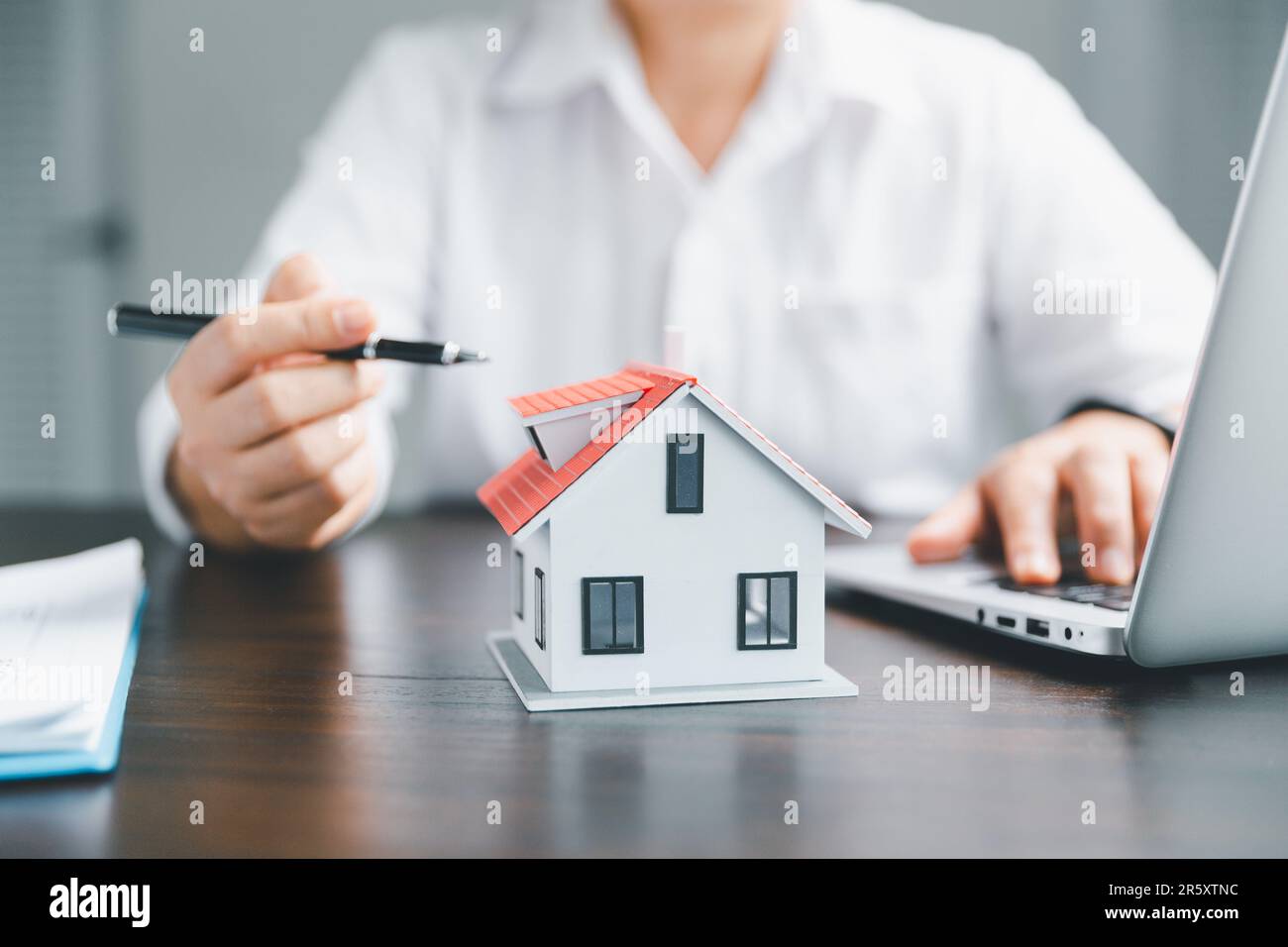 Los agentes inmobiliarios ofrecen contratos de compra o alquiler residencial. Manos de la persona de negocios con el modelo casero, pequeña casa roja del edificio. Propiedad hipotecaria Foto de stock