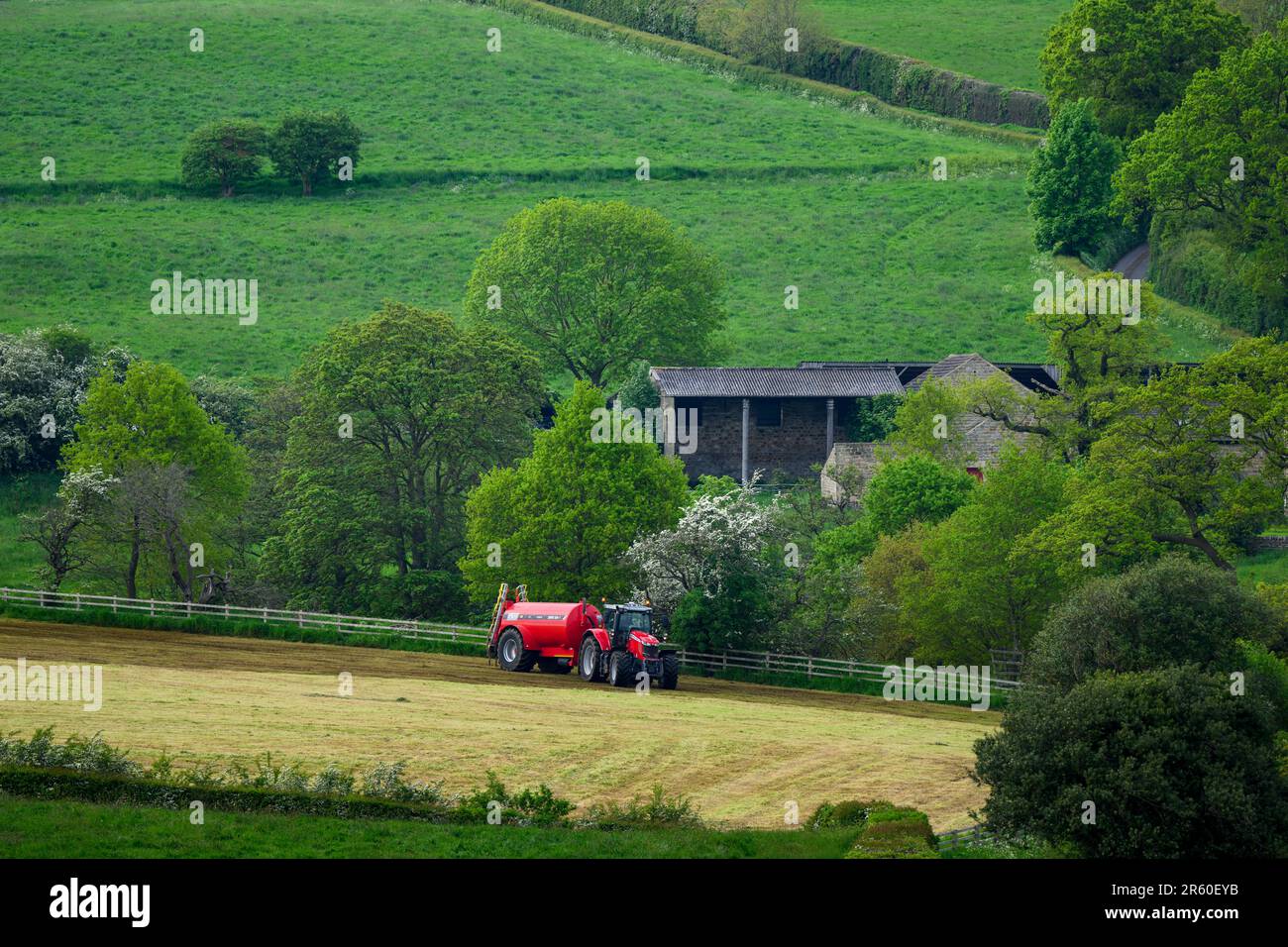 Agricultor trabajando con tractor de conducción y tanque de fertilizante cilíndrico rociando con purina descarga en campo agrícola pasto - Yorkshire, Inglaterra, Reino Unido Foto de stock