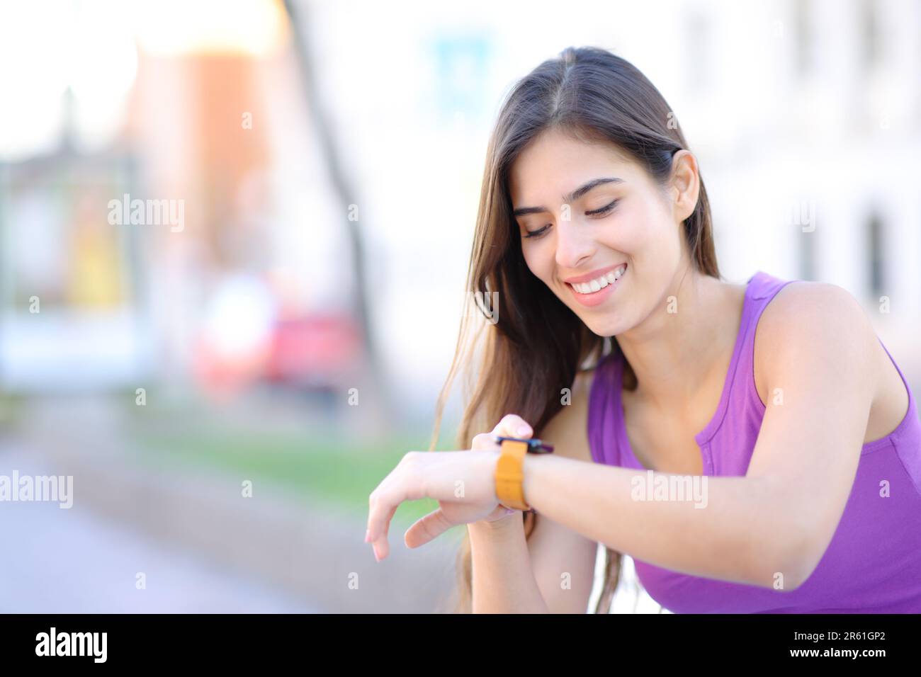 Mujer feliz usando su smartwath sentado en un banco en la calle Foto de stock