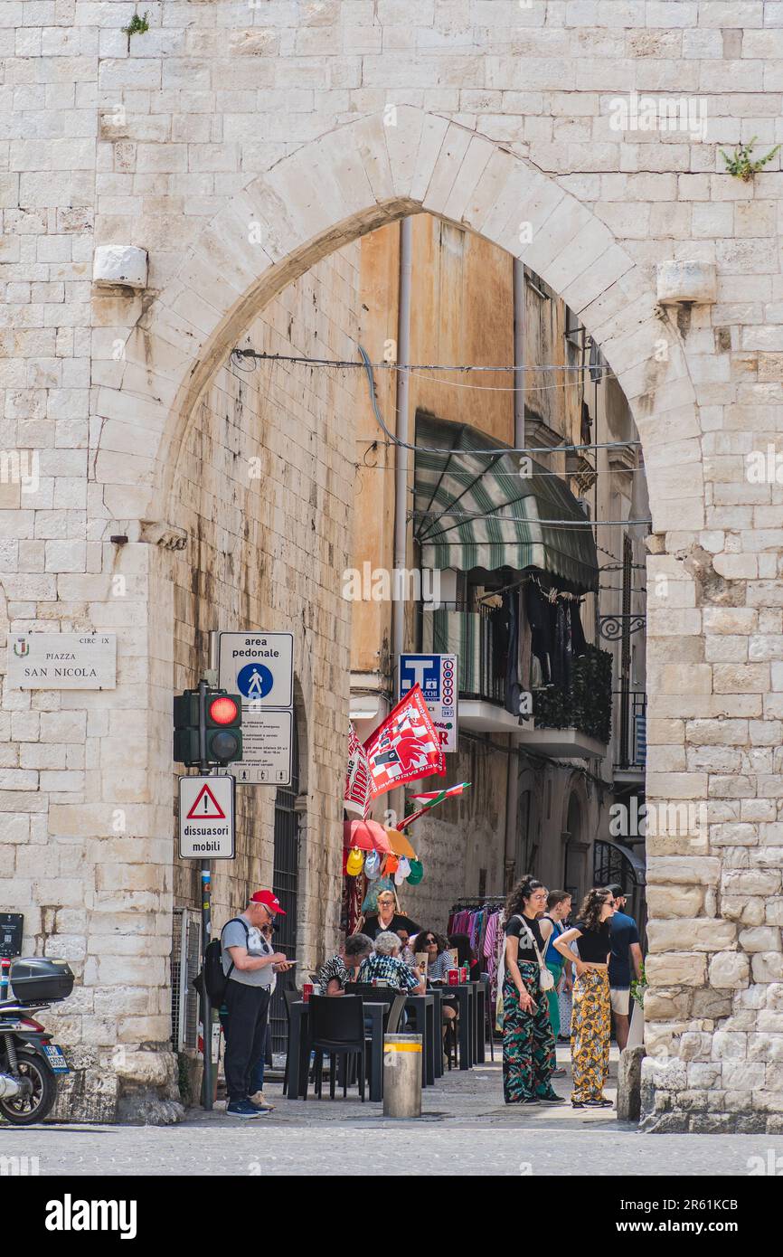 Puerta medieval, antiguas paredes de piedra y calle estrecha en el casco antiguo de Bari, Puglia, Italia con los turistas que caminan cerca, vertical Foto de stock
