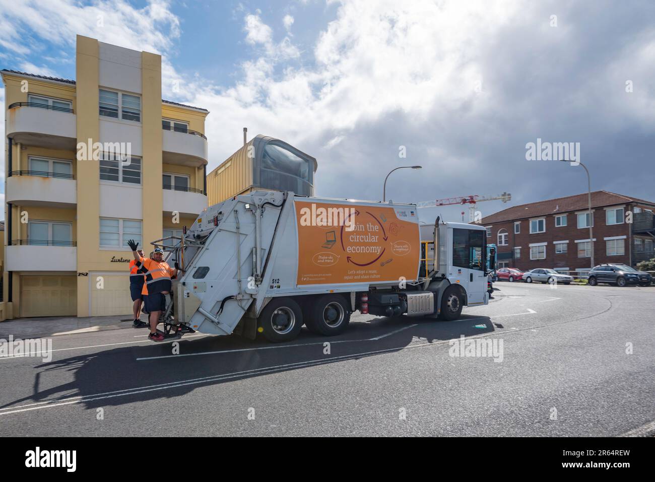 Dos recolectores de basura felices agitando y montando en la parte trasera de un camión en Campbell Parade, North Bondi, Sydney, Australia Foto de stock