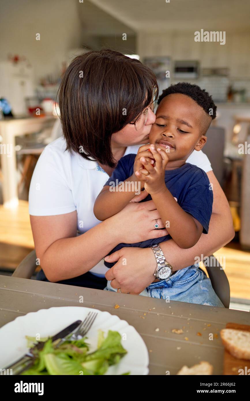 Madre besando lindo hijo comiendo en la mesa de la cena Foto de stock