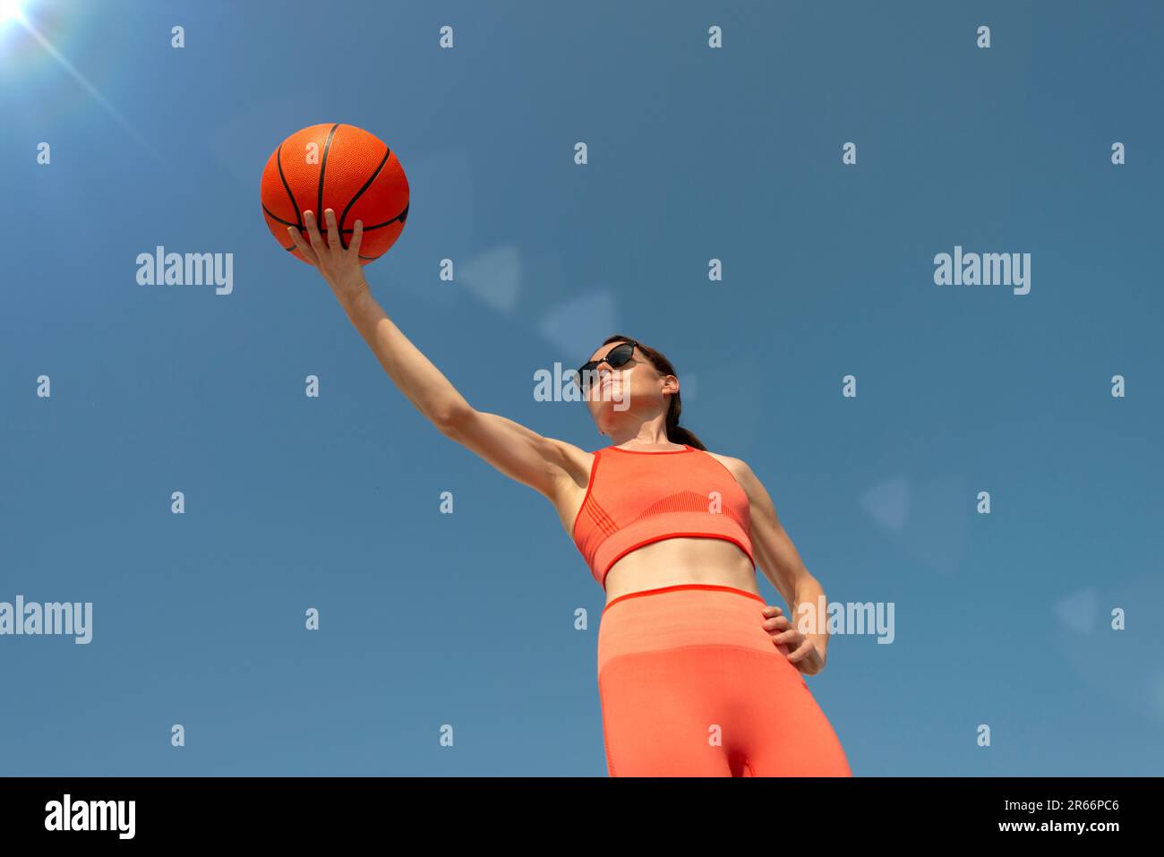 Mujer deportiva, en forma sosteniendo un fondo de baloncesto, cielo azul. Foto de stock