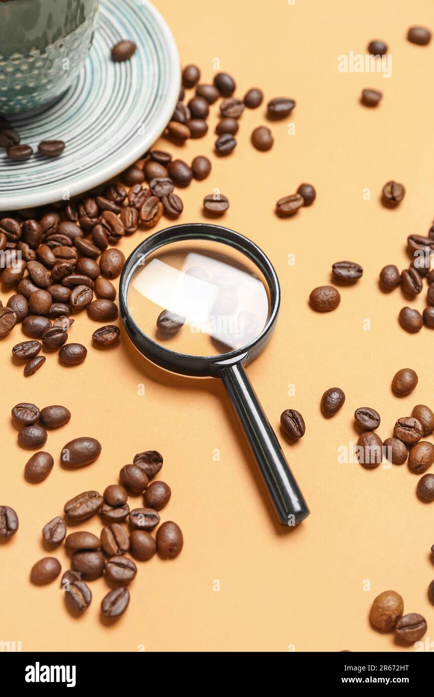 Lupa y taza de café con granos sobre fondo naranja pálido Fotografía de  stock - Alamy