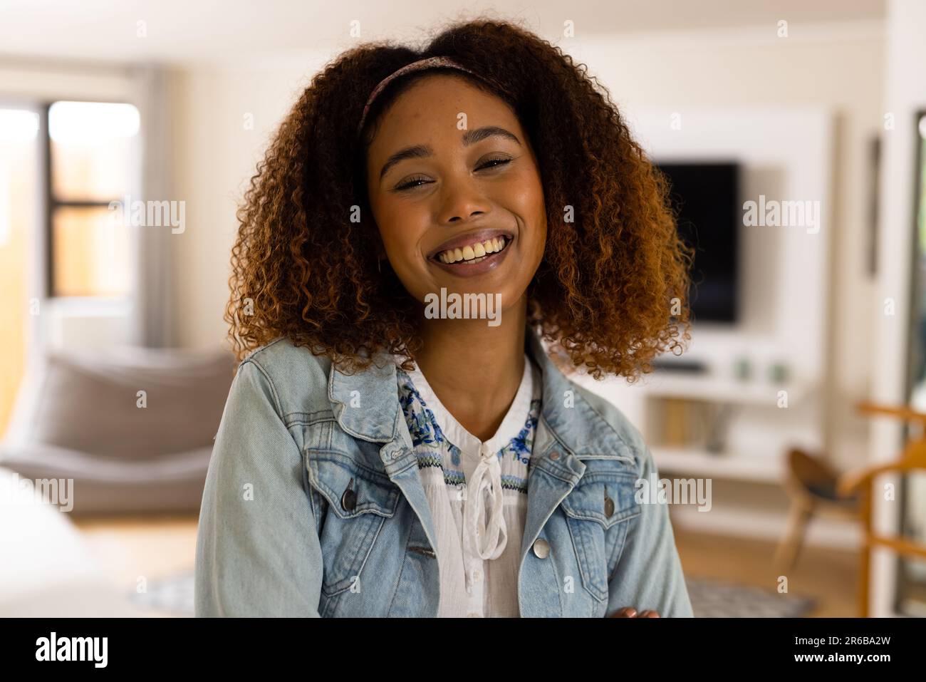 Retrato de mujer biracial feliz con el pelo rizado sonriendo a la cámara en casa Foto de stock