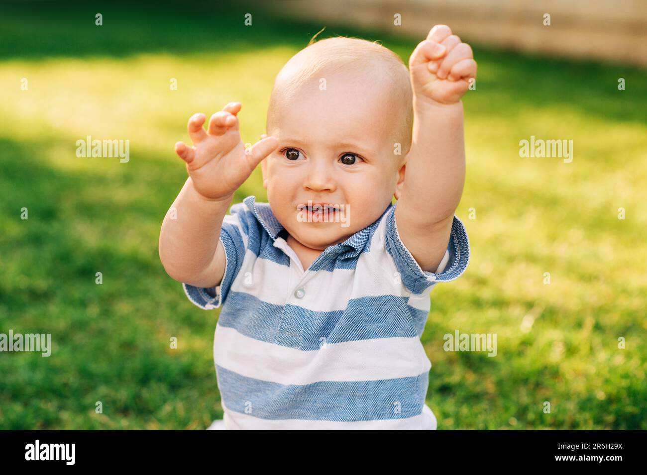 Retrato al aire libre del bebé adorable que juega en el parque del verano, tirando de las manos hacia arriba Foto de stock