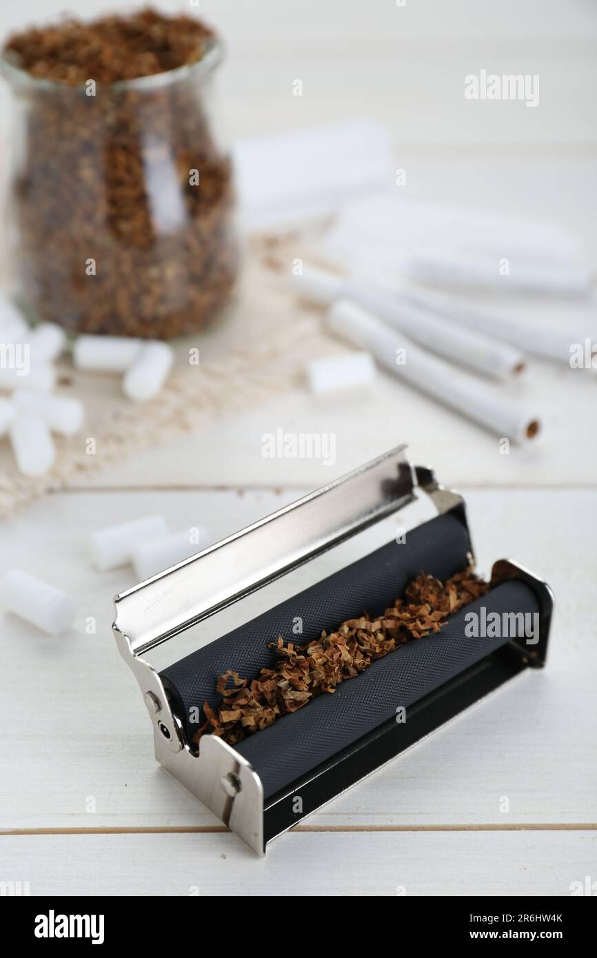 Rodillo con tabaco en mesa de madera blanca. Hacer cigarrillos enrollados a mano Foto de stock