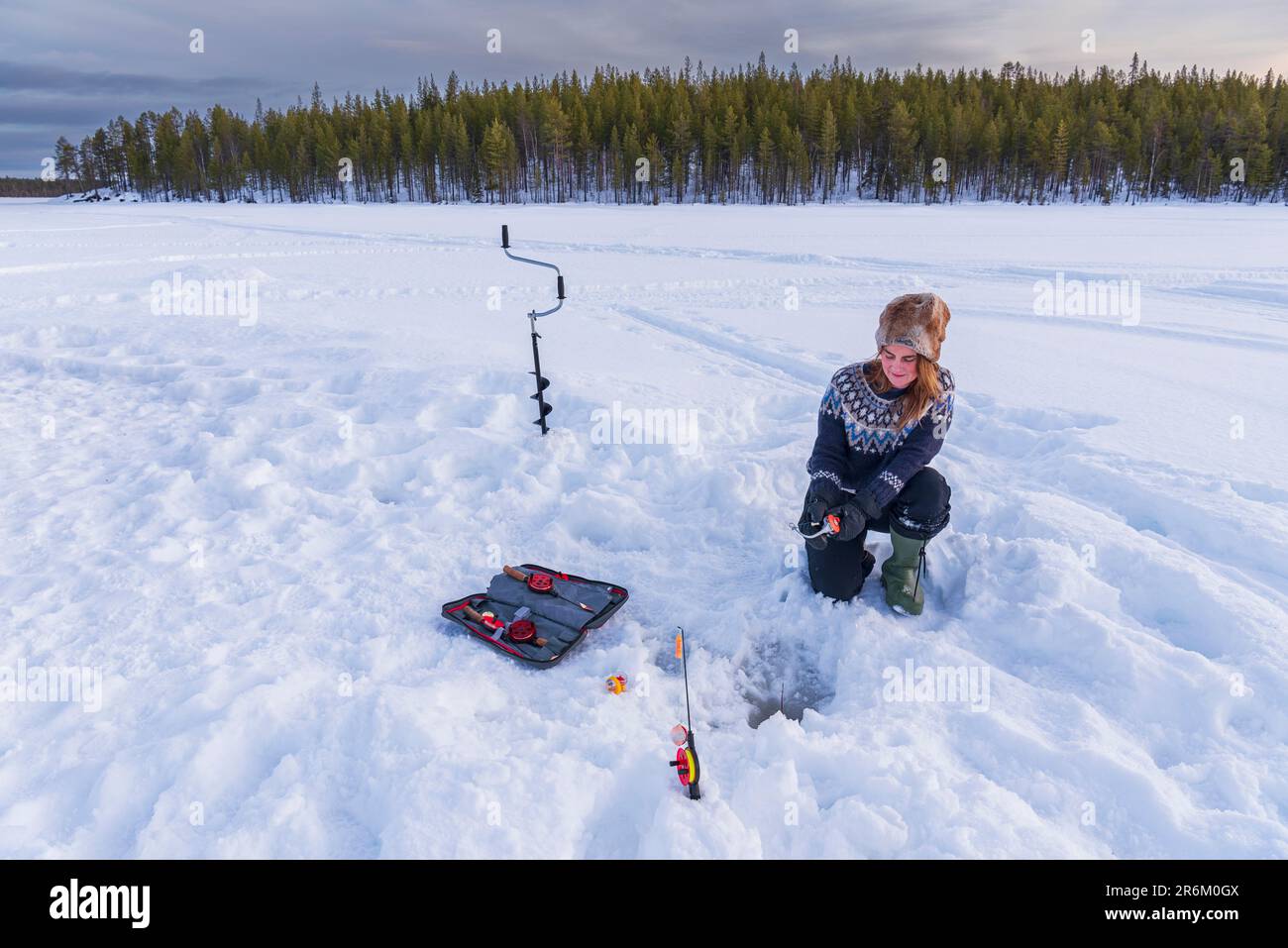 Mujer en ropa escandinava pesca en hielo en un lago congelado, Laponia, Suecia, Escandinavia, Europa Foto de stock