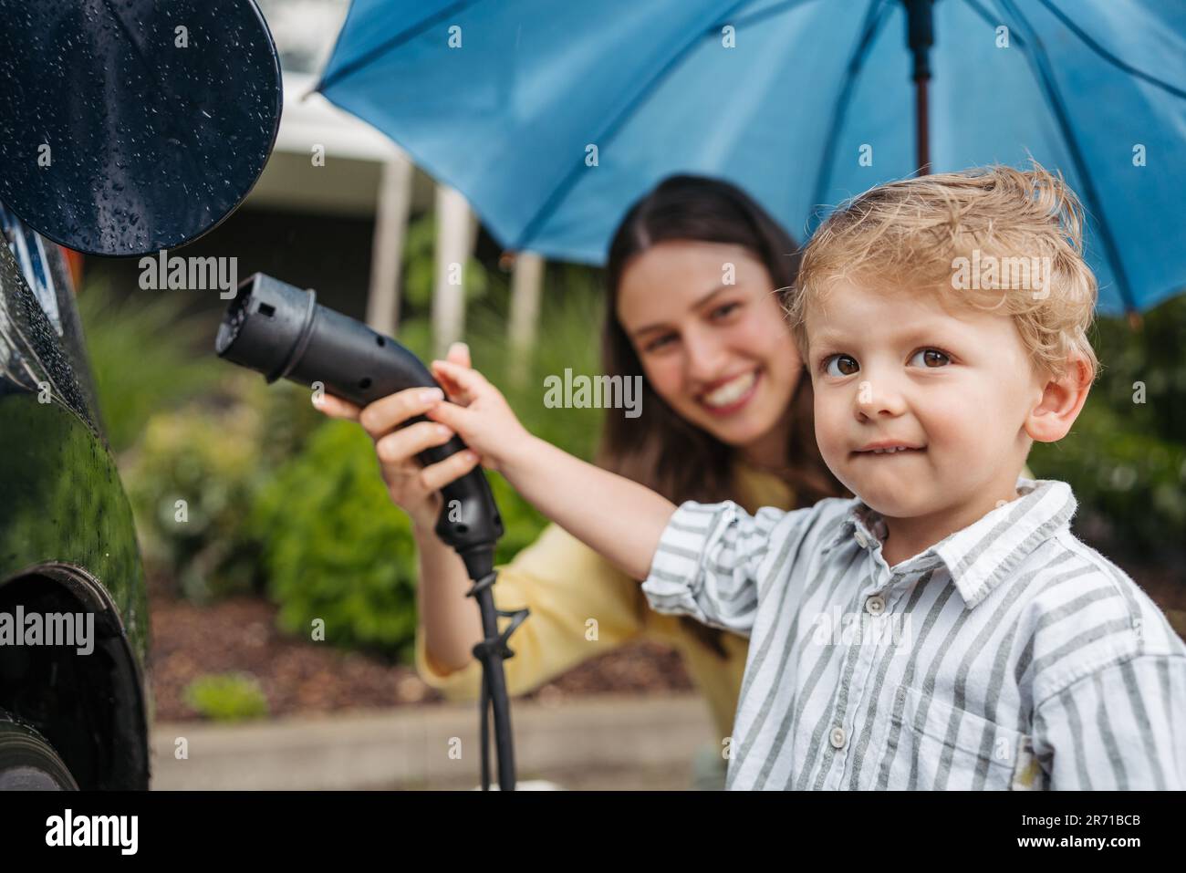 Cerca de la madre sonriente y su pequeño hijo cargando su coche eléctrico  en un día lluvioso, de pie debajo del paraguas Fotografía de stock - Alamy