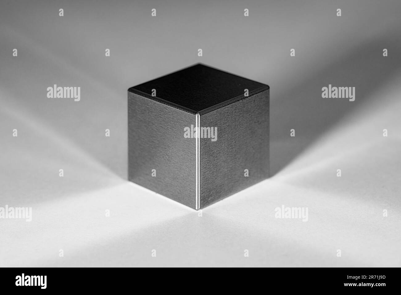 Un cubo de tungsteno con reflejos y sombras sobre un fondo blanco Foto de stock
