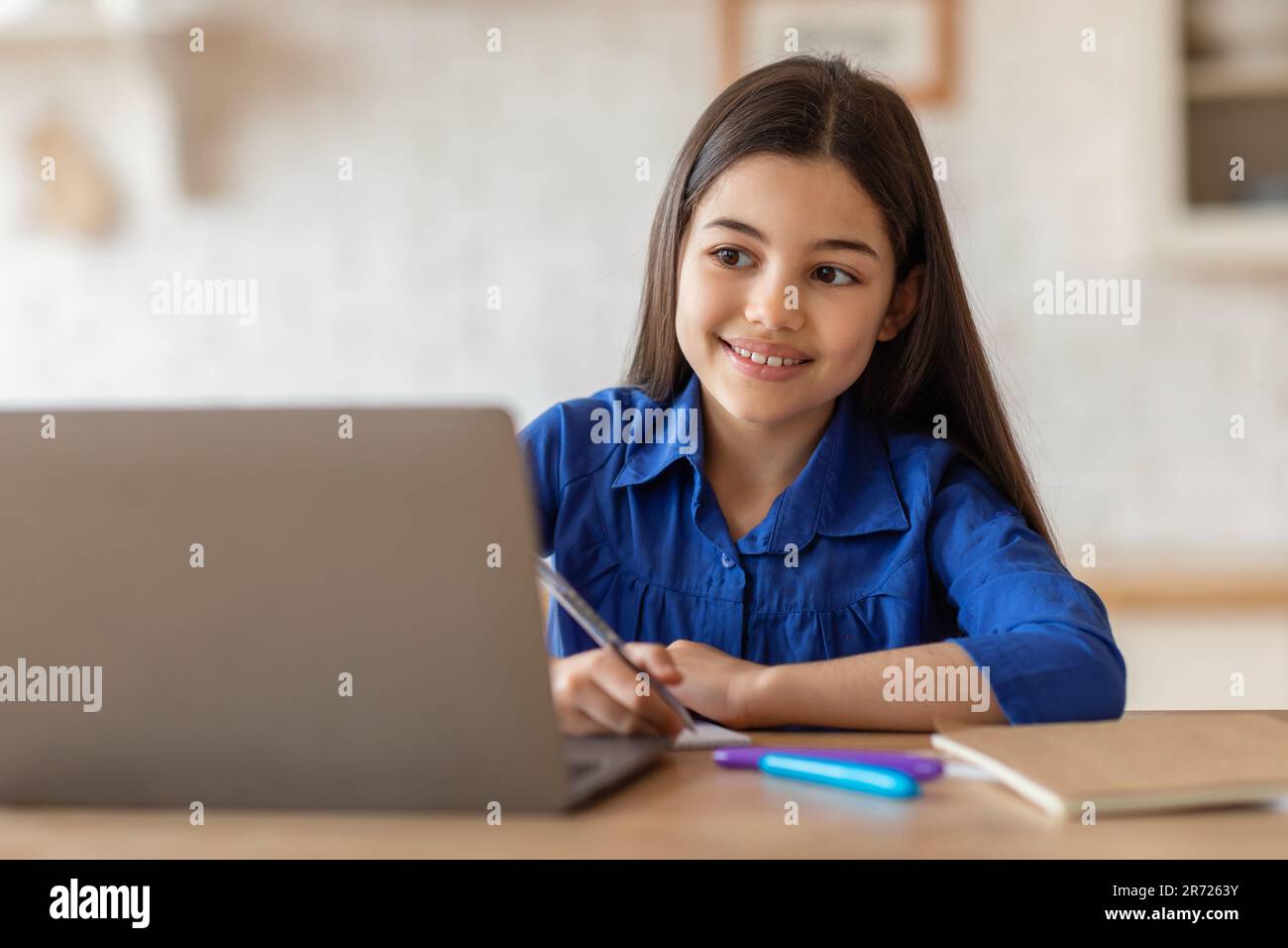 Sonriente colegiala escribiendo notas mirando el ordenador portátil que estudia en casa Foto de stock